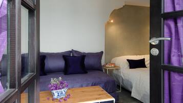 A room with a sofa, a small table with a vase, a bed, and a nightstand.