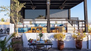 Une terrasse sur le toit, avec une table à manger dressée pour le petit-déjeuner, des plantes en pot et une vue sur le paysage urbain.