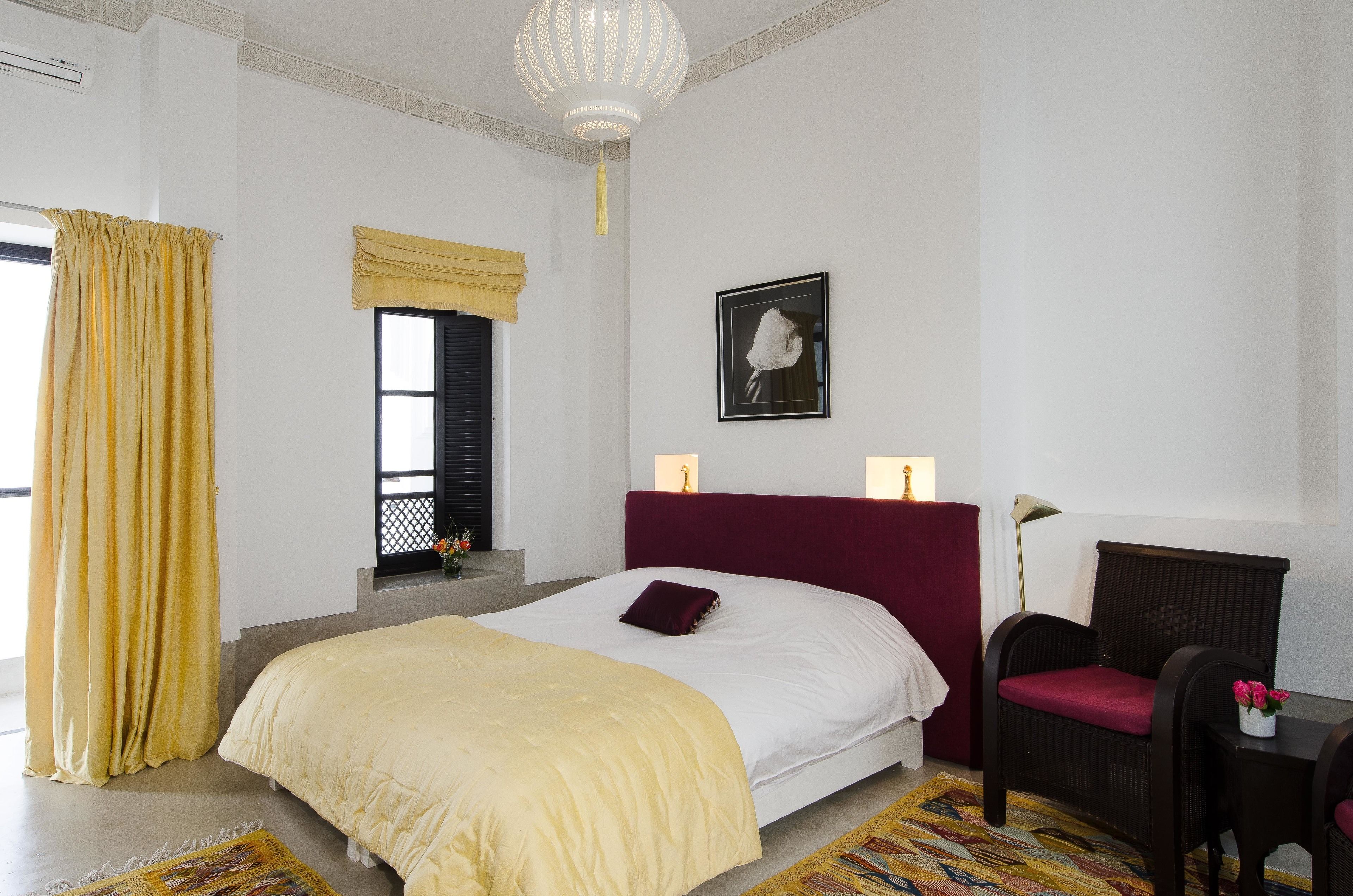 Um quarto com uma cama grande, uma cadeira, uma escrivaninha, uma luminária e um quadro na parede.