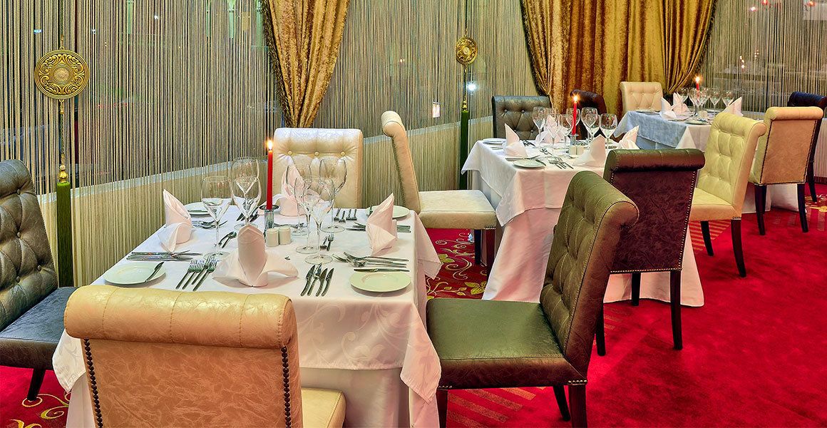Une salle à manger élégante, avec des tables dressées pour accueillir de nombreux convives, dotée de sièges confortables et d’un tapis rouge.