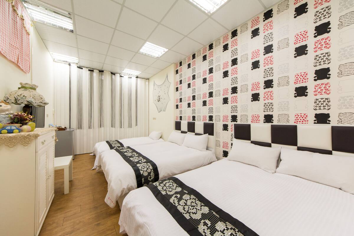 A hotel room with two beds, a small desk, and a decorative wall.