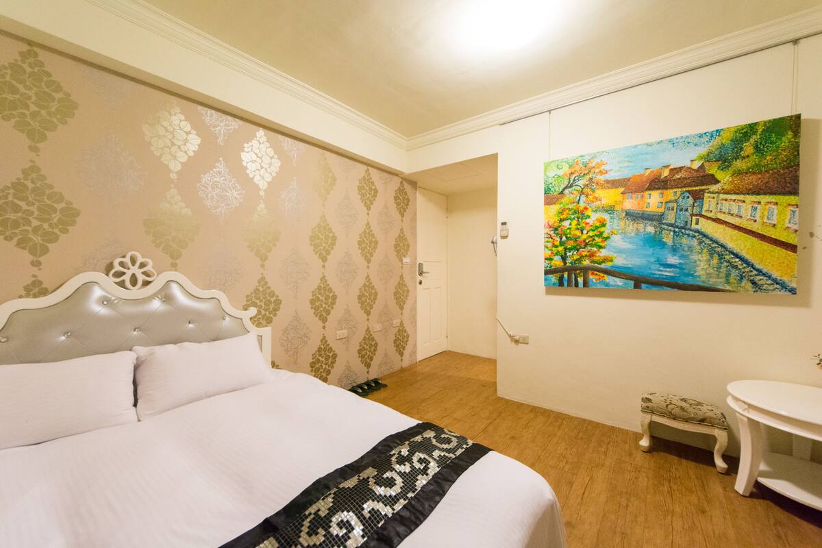 A hotel room with a bed, a small table, a bench, and a painting on the wall.