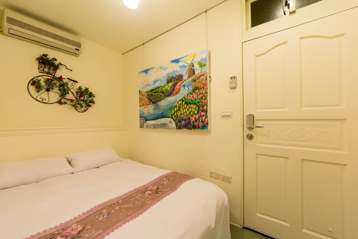 A bedroom with a bed, a painting of a landscape, a bicycle decoration, and a door.