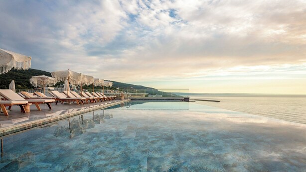 An infinity pool with lounge chairs and umbrellas, overlooking a body of water and hills. - Grifid Hotel Vistamar - Ultra All Inclusive (Golden Sands)