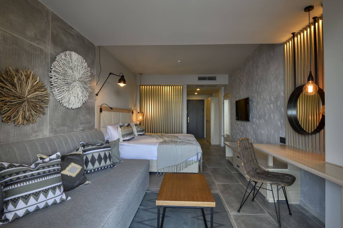 A modern hotel room with a bed, sofa, and a dining area.