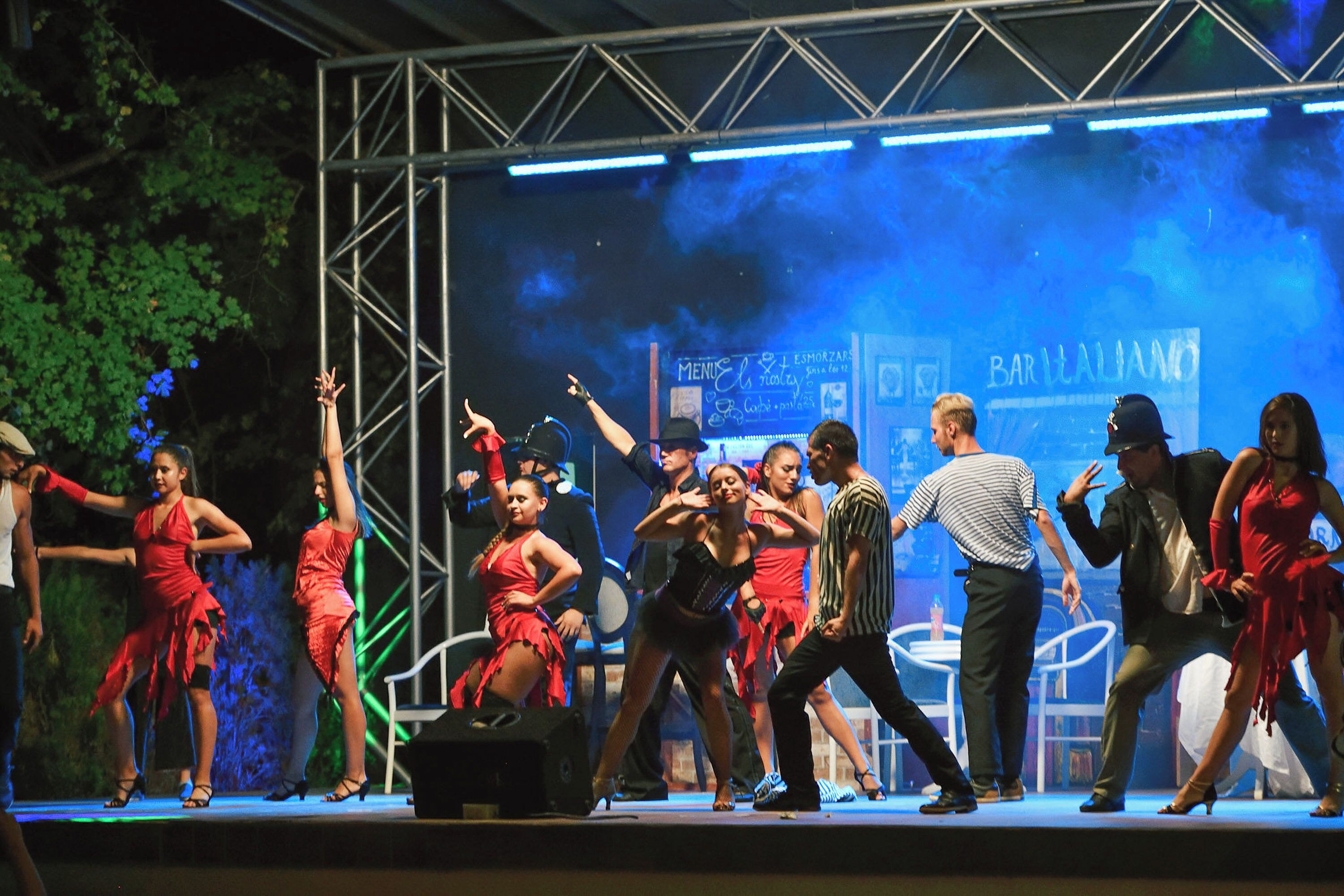 A stage with performers in red dresses, a metal truss structure, and a blue background with text.