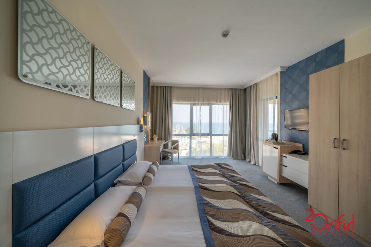 A hotel room with a large bed, a desk, a TV, and a view of the city.