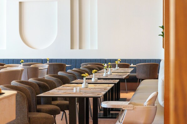 Un restaurant avec de longues tables, des chaises et des vases remplis de fleurs.