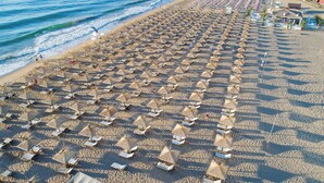 Ein Strand mit Reihen von Sonnenschirmen und Liegestühlen, ein sandiger Strand und das Meer im Hintergrund.