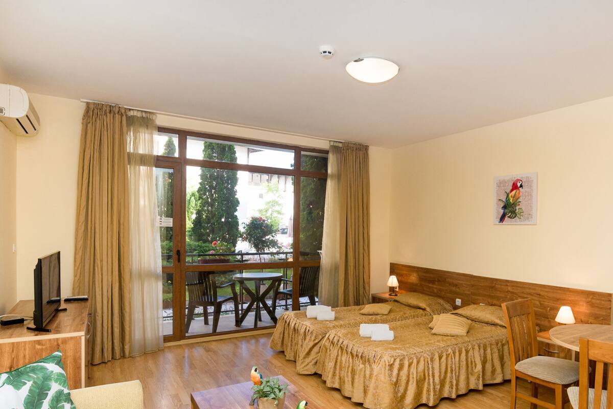 A hotel room with a bed, a small table, a chair, a TV, and a window with curtains.