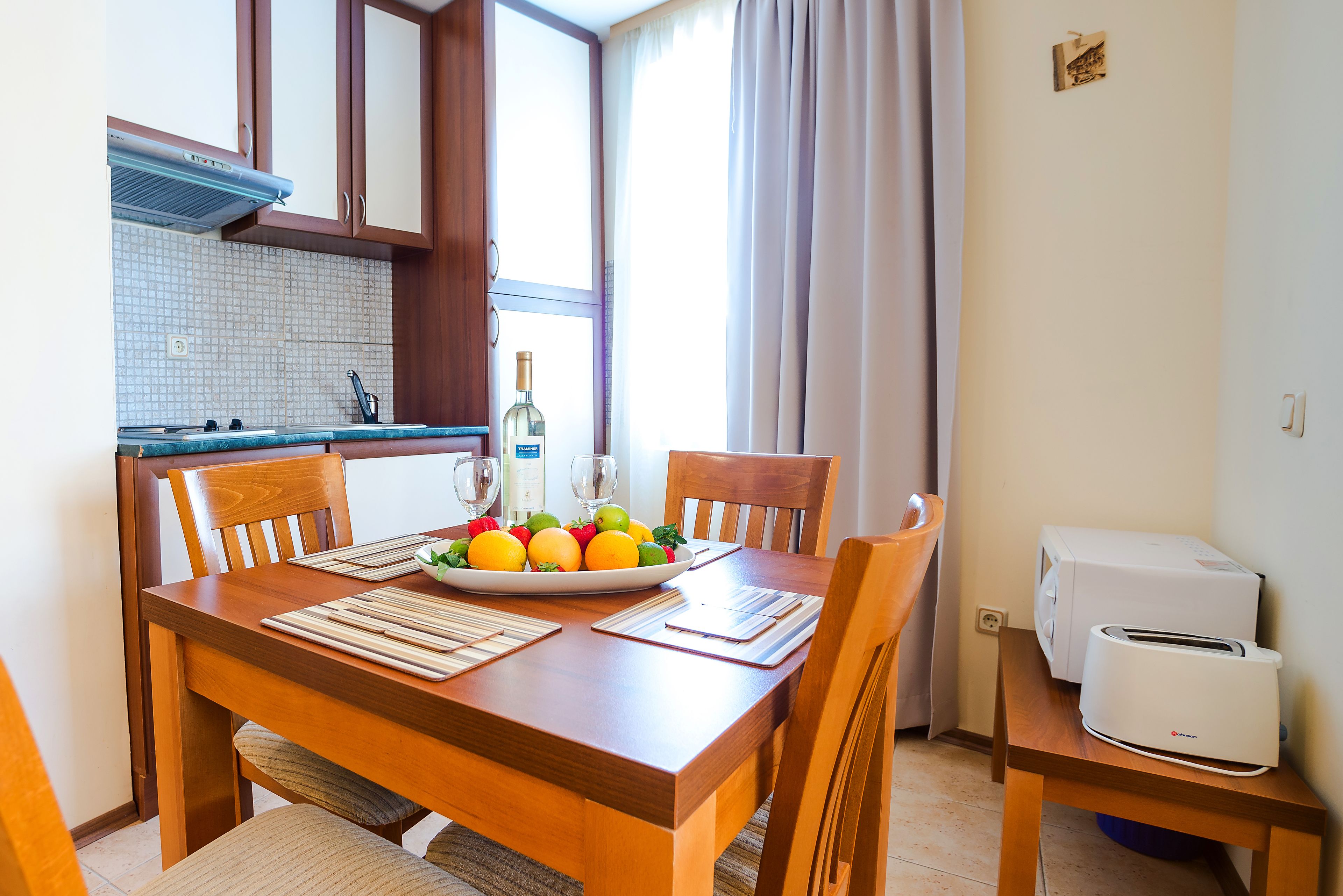 A dining table with a fruit bowl, wine bottle, and glasses, a toaster, and a microwave on a small table beside it.