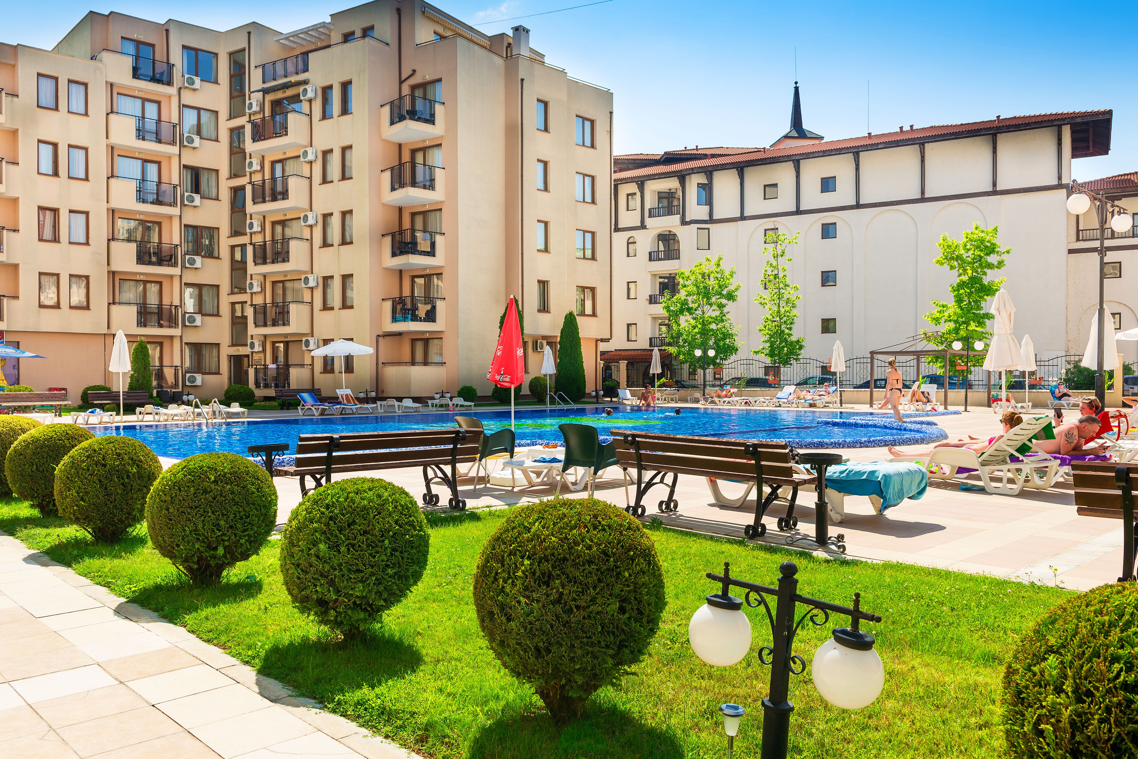 Un hotel con piscina, mobiliario exterior y arbustos bien cuidados.