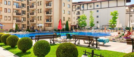 Un hotel con piscina, mobiliario exterior y arbustos bien cuidados.