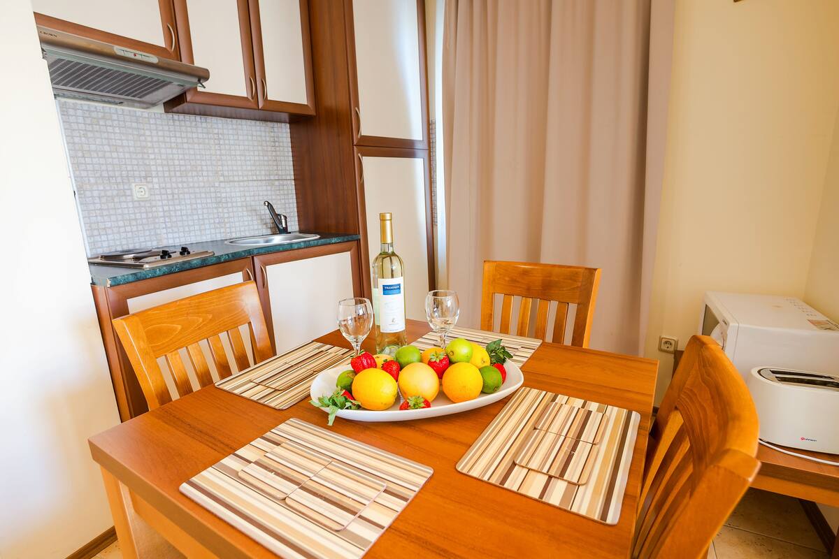 A wooden dining table with a plate of fruit, two wine glasses, and a bottle of wine.