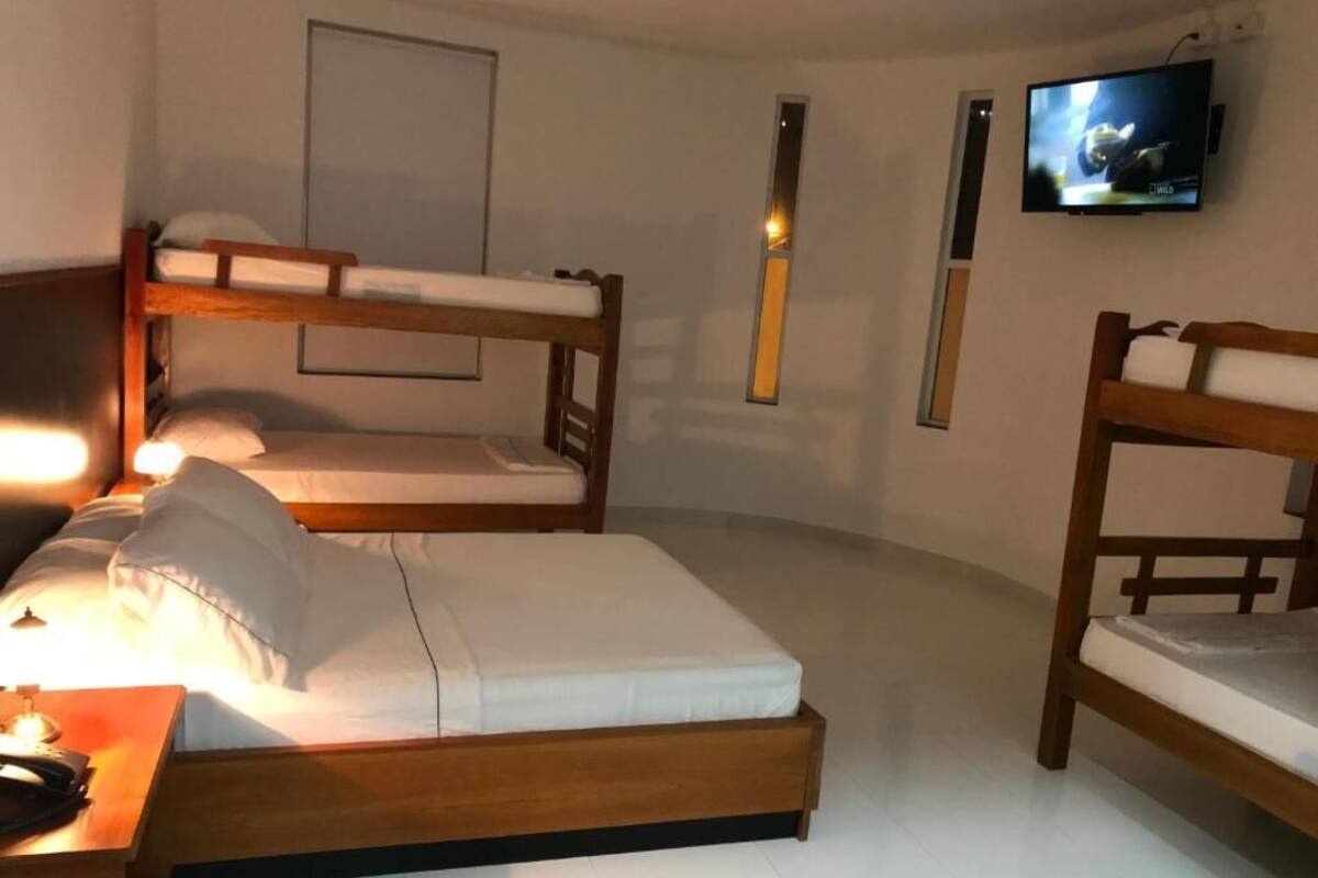 Una habitación con dos literas, una mesita de noche con lámpara, y un televisor montado en la pared.