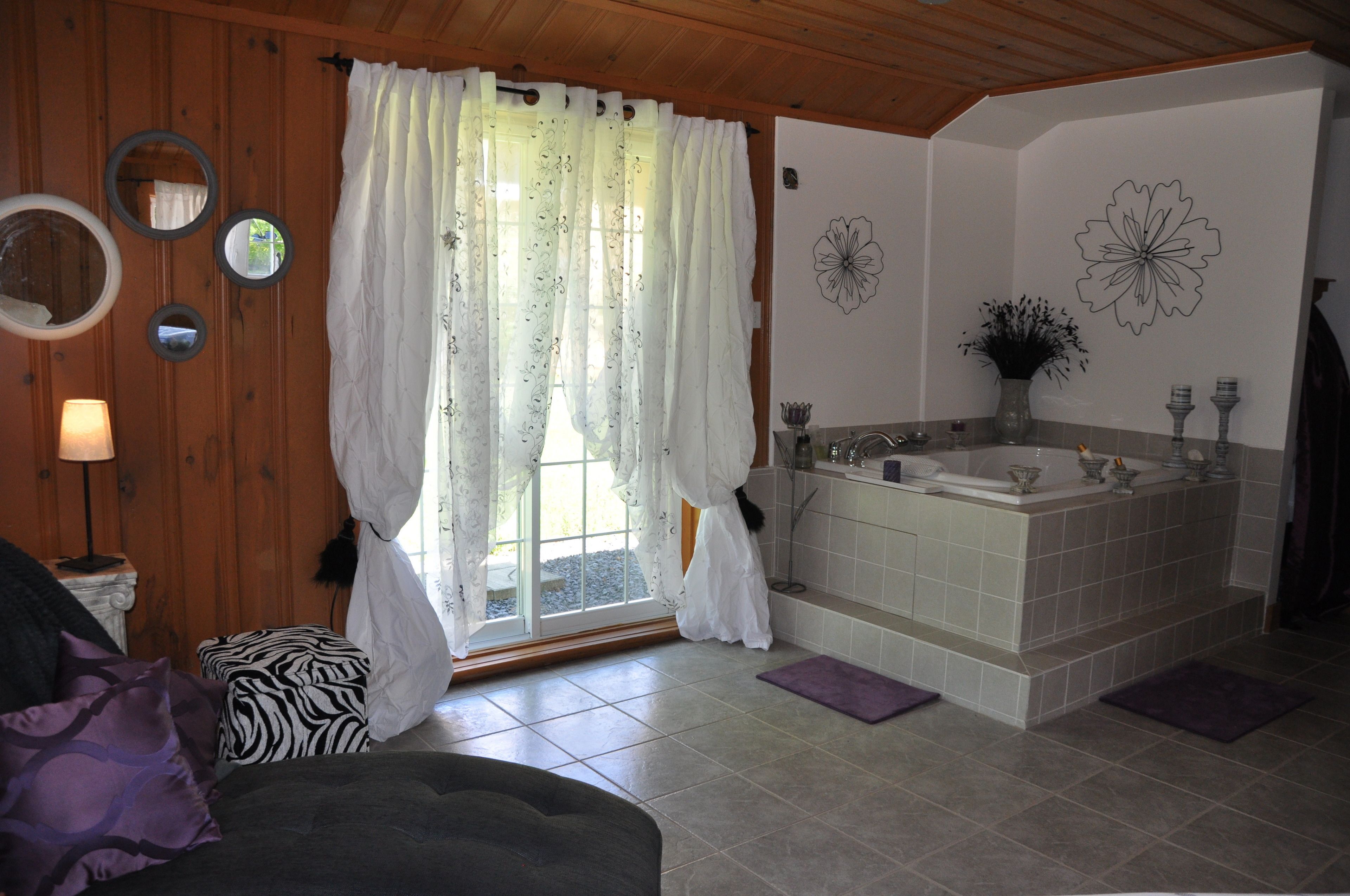 Un baño con bañera, una ventana con cortinas, un espejo y un adorno de pared.