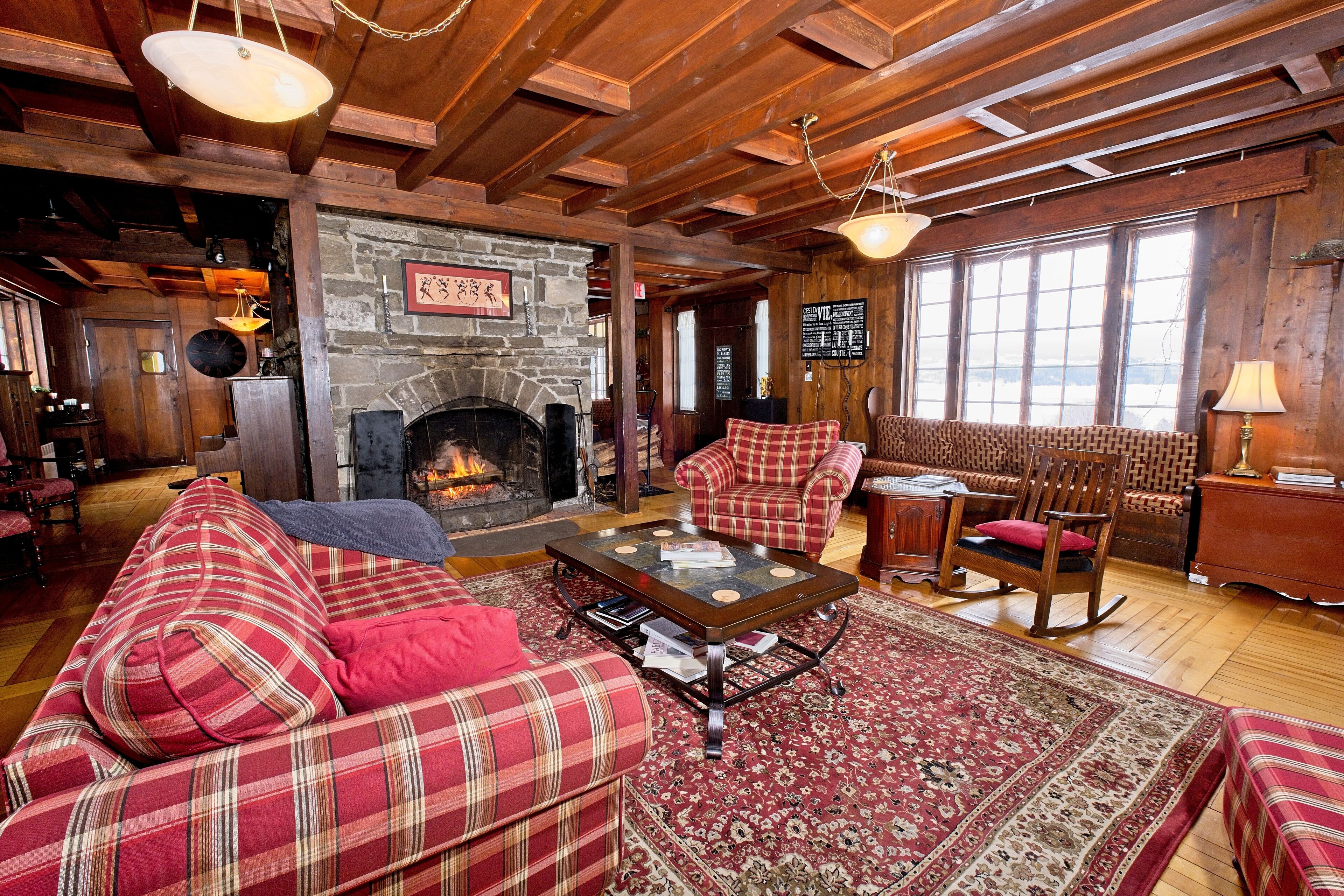 A cozy living room with a fireplace, plaid furniture, and a large window.