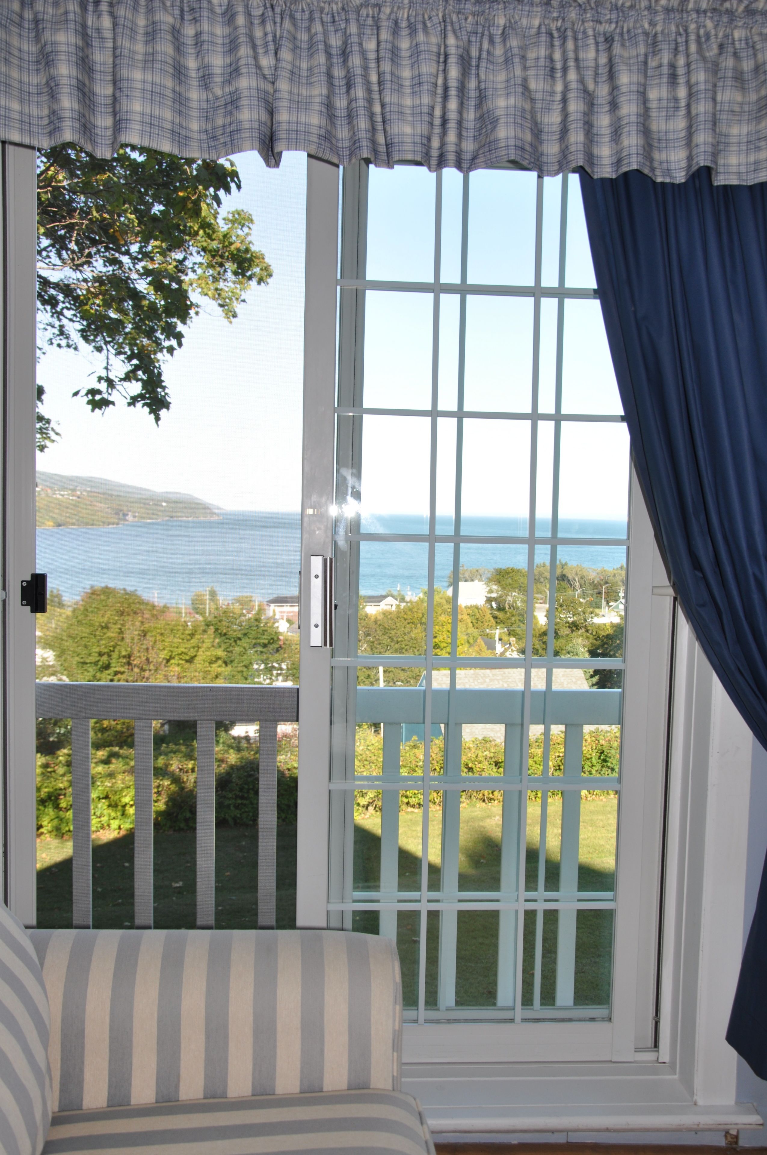 Una habitación con vista al mar a través de una ventana con contraventanas blancas.