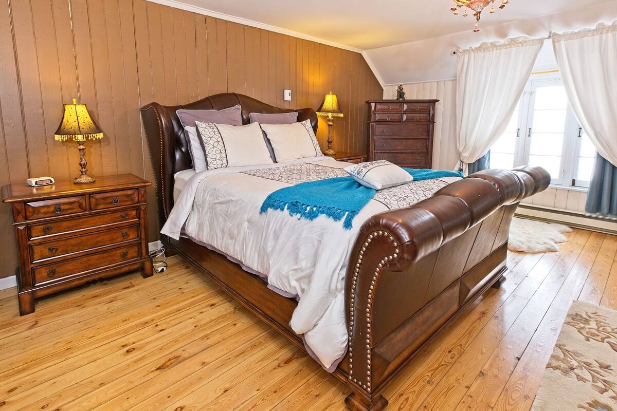 A bedroom with a wooden bed, two bedside tables with lamps, a dresser, and a window with curtains.
