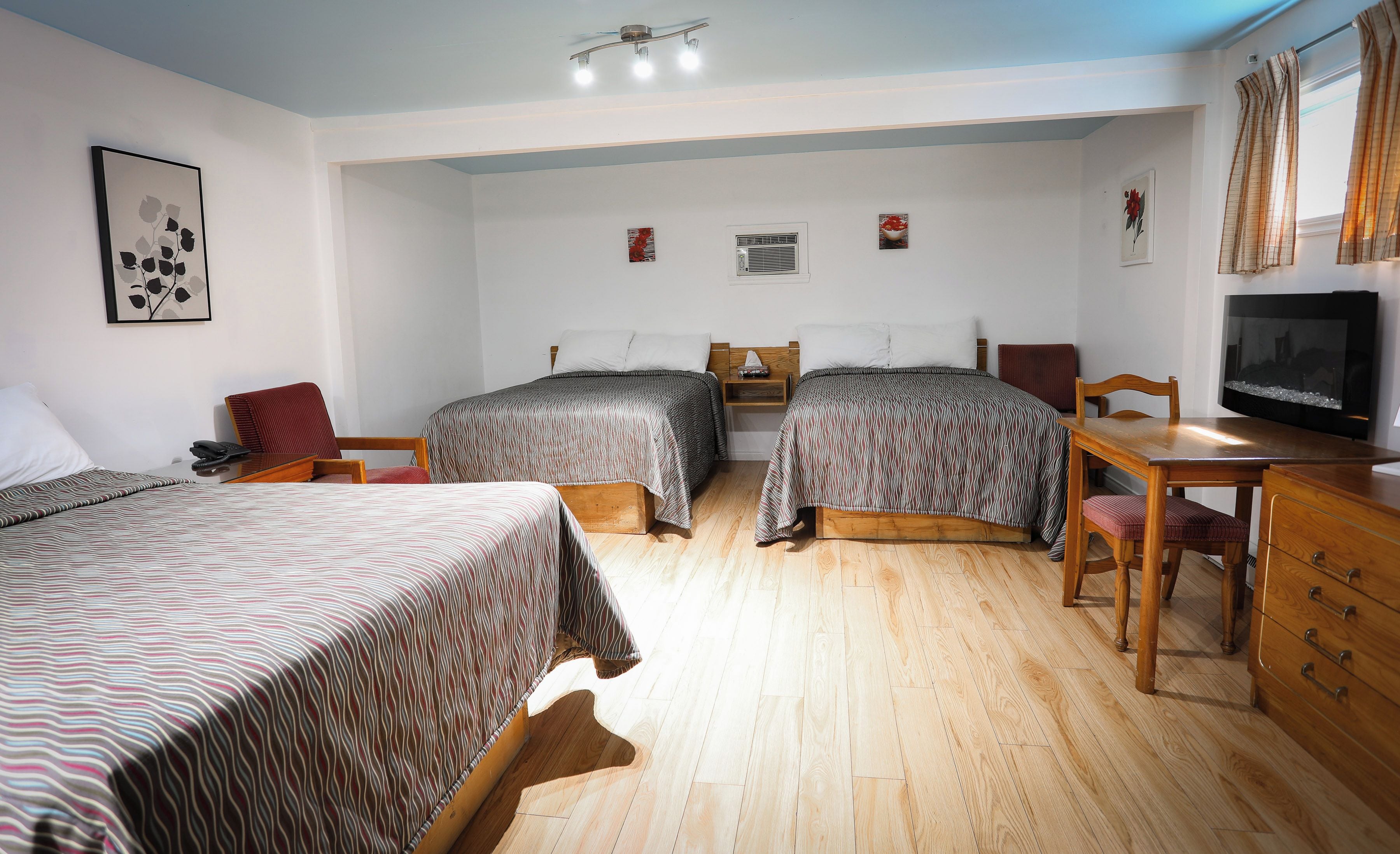 A hotel room with two beds, a wooden desk, a television, and a ceiling fan.