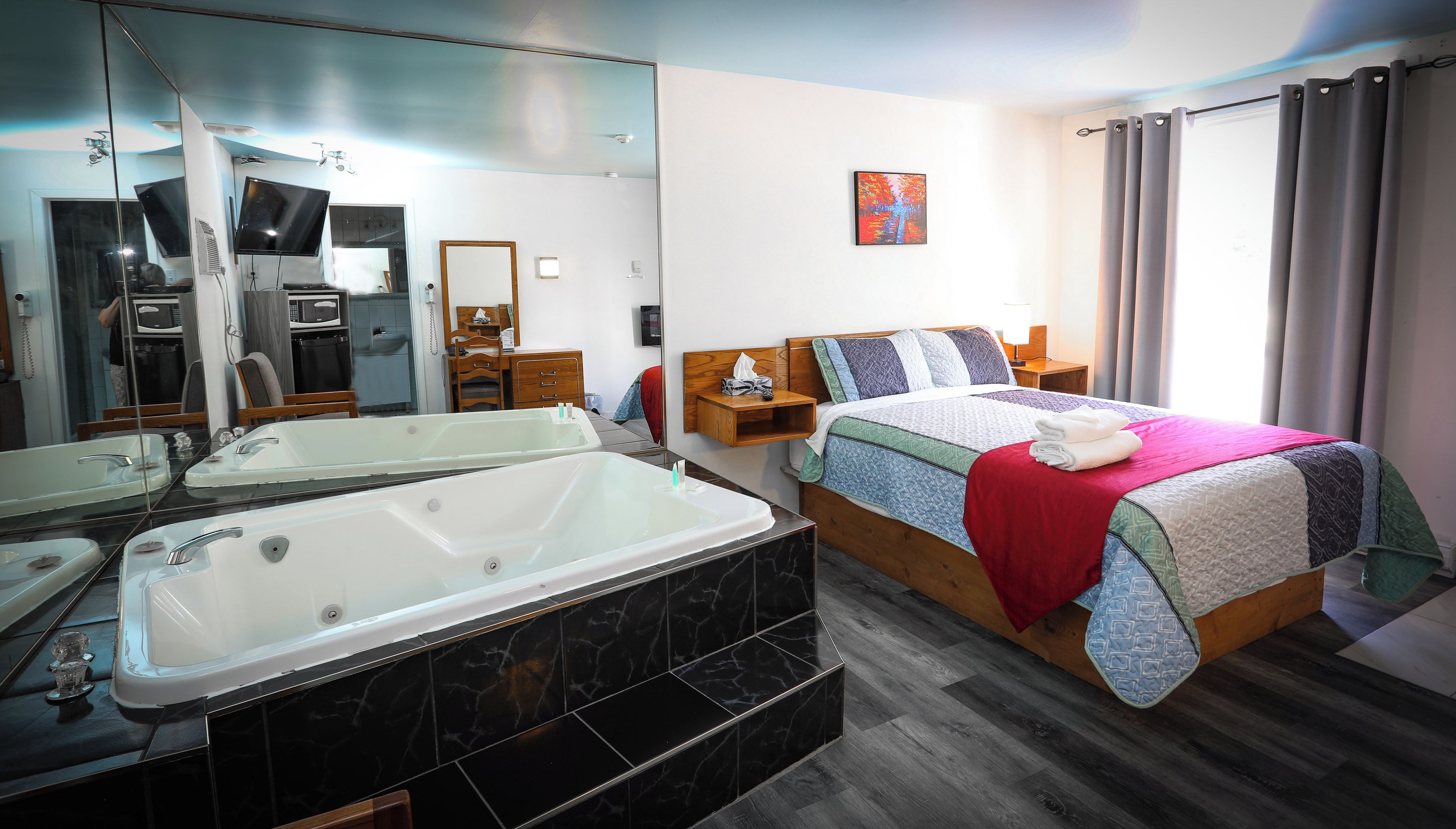 Habitación de hotel con una bañera grande, cama con manta roja y cabecera de madera.