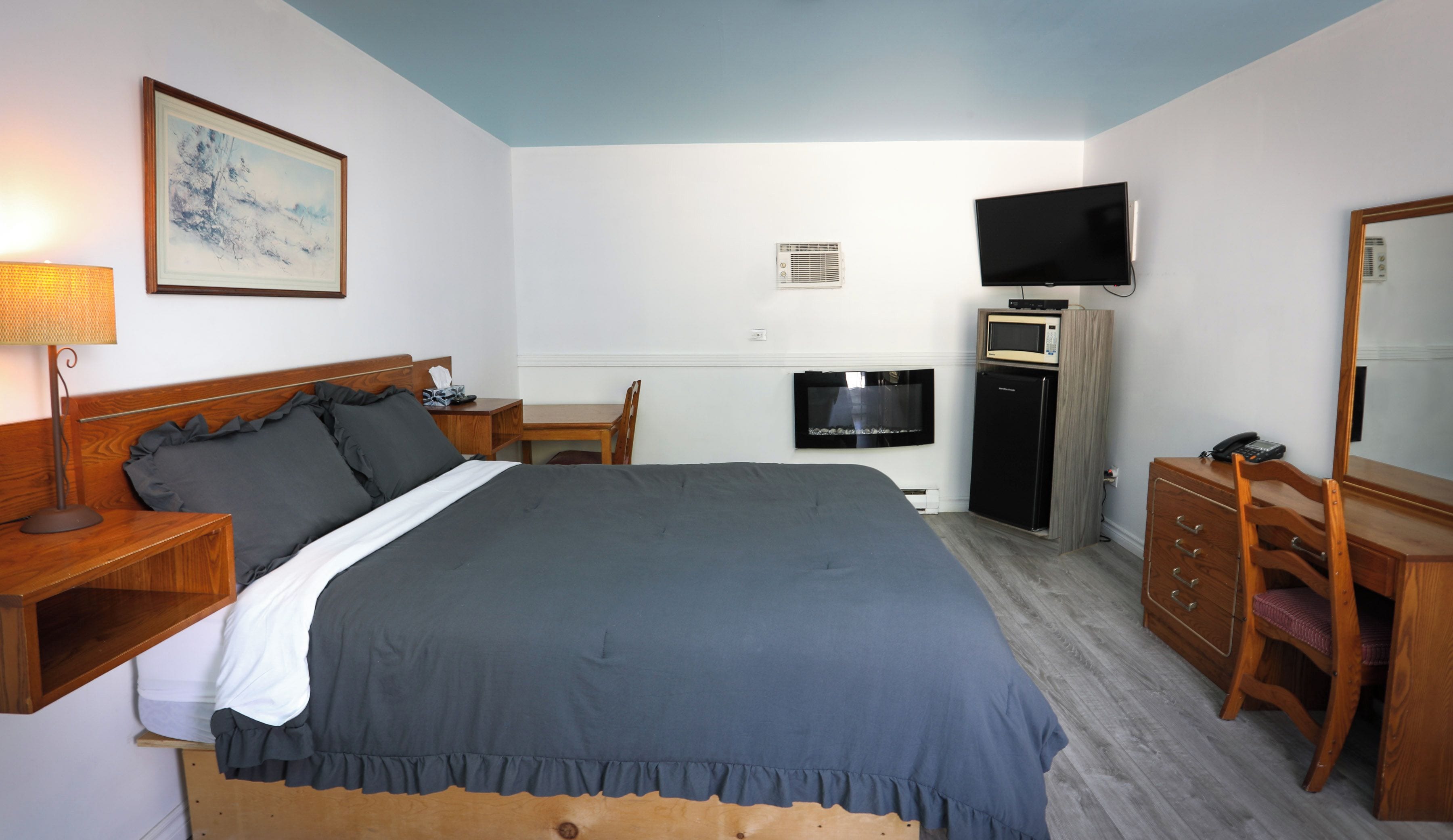 Habitación de hotel con cama, escritorio, silla, televisor, microondas, refrigerador y cómoda.