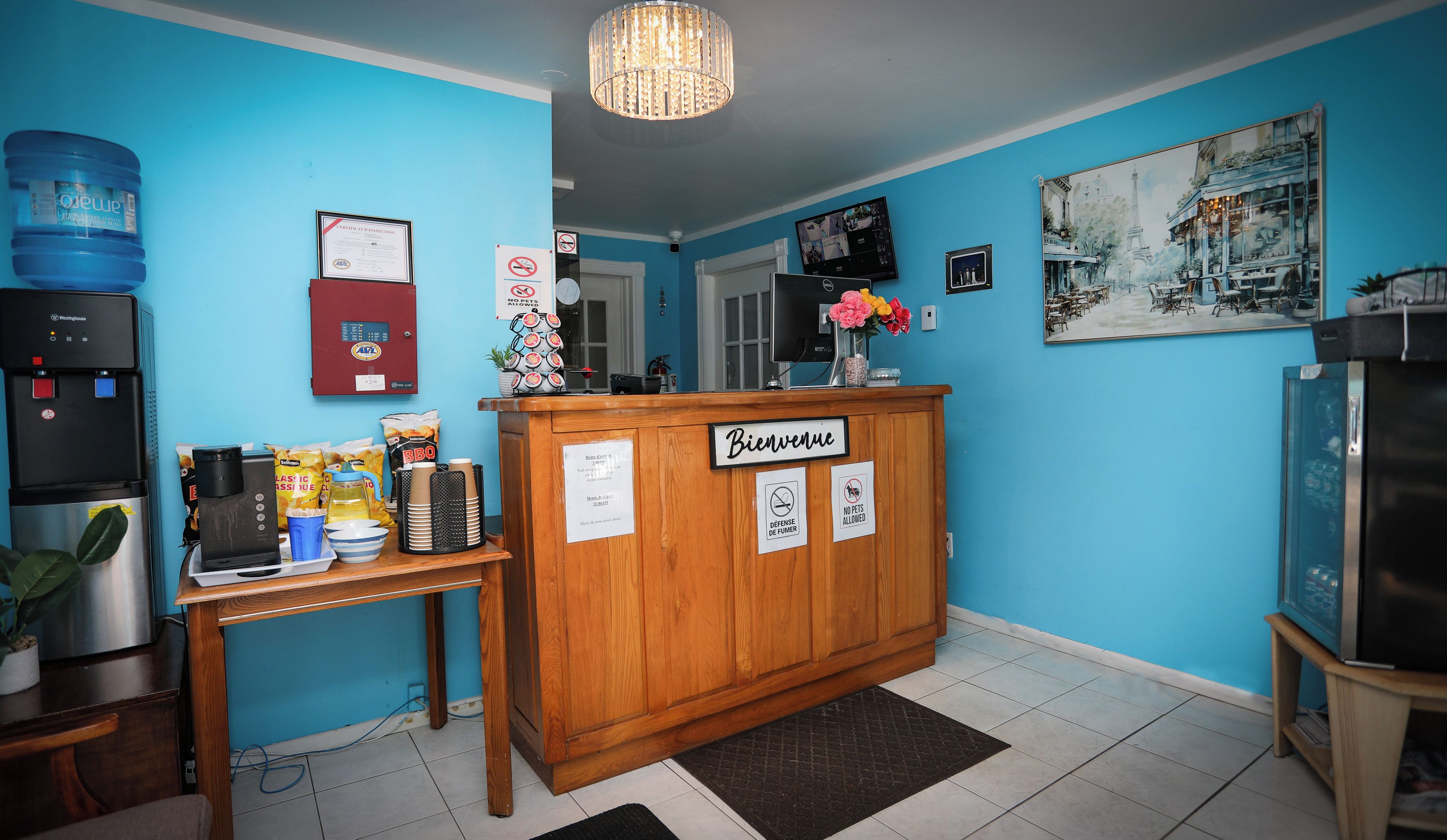 Een receptiegedeelte met een houten balie, een waterdispenser, een koffieapparaat en een bordje met de tekst 'Bienvenue'.