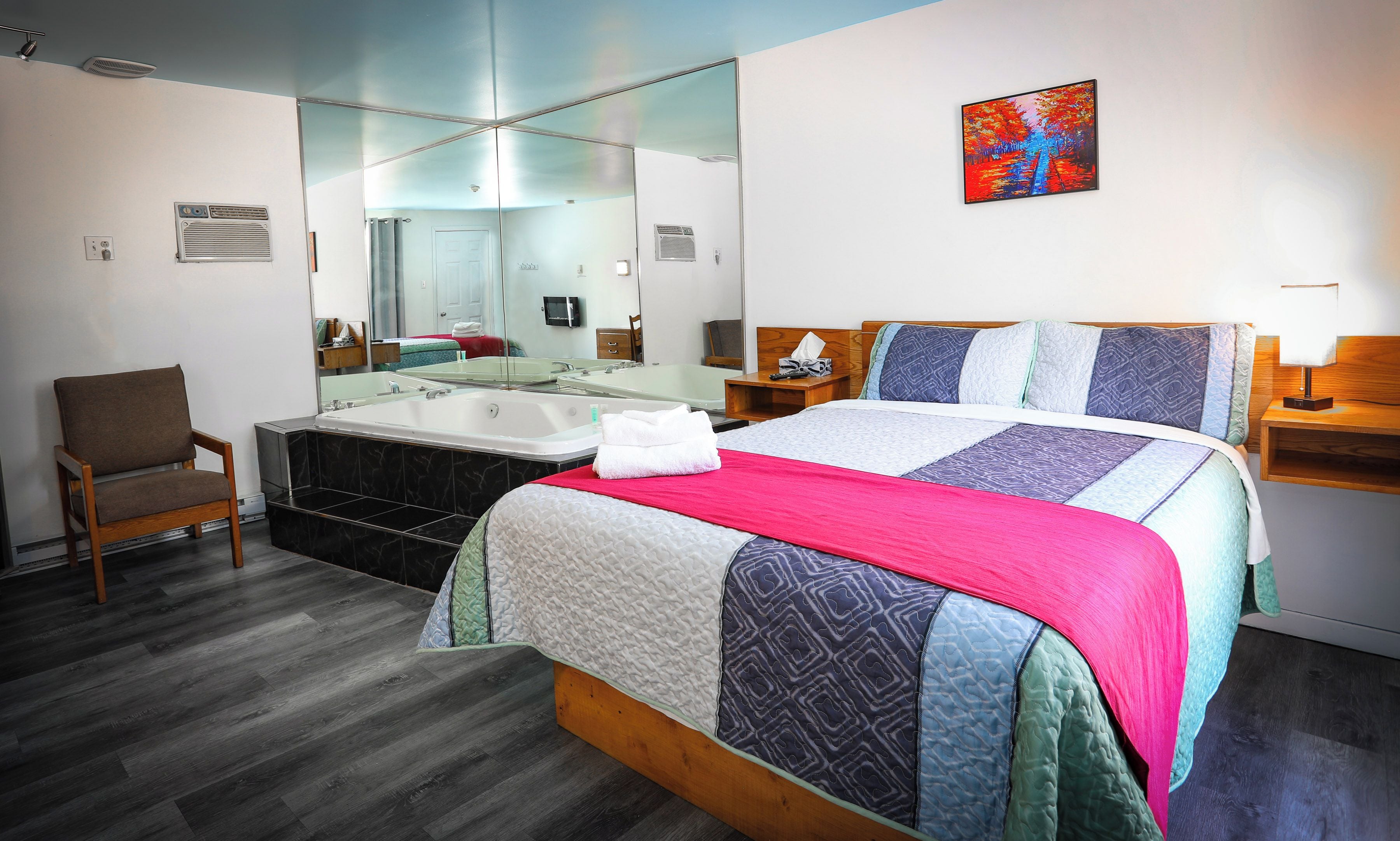A hotel room with a bed, a chair, a bathtub, and a painting on the wall.