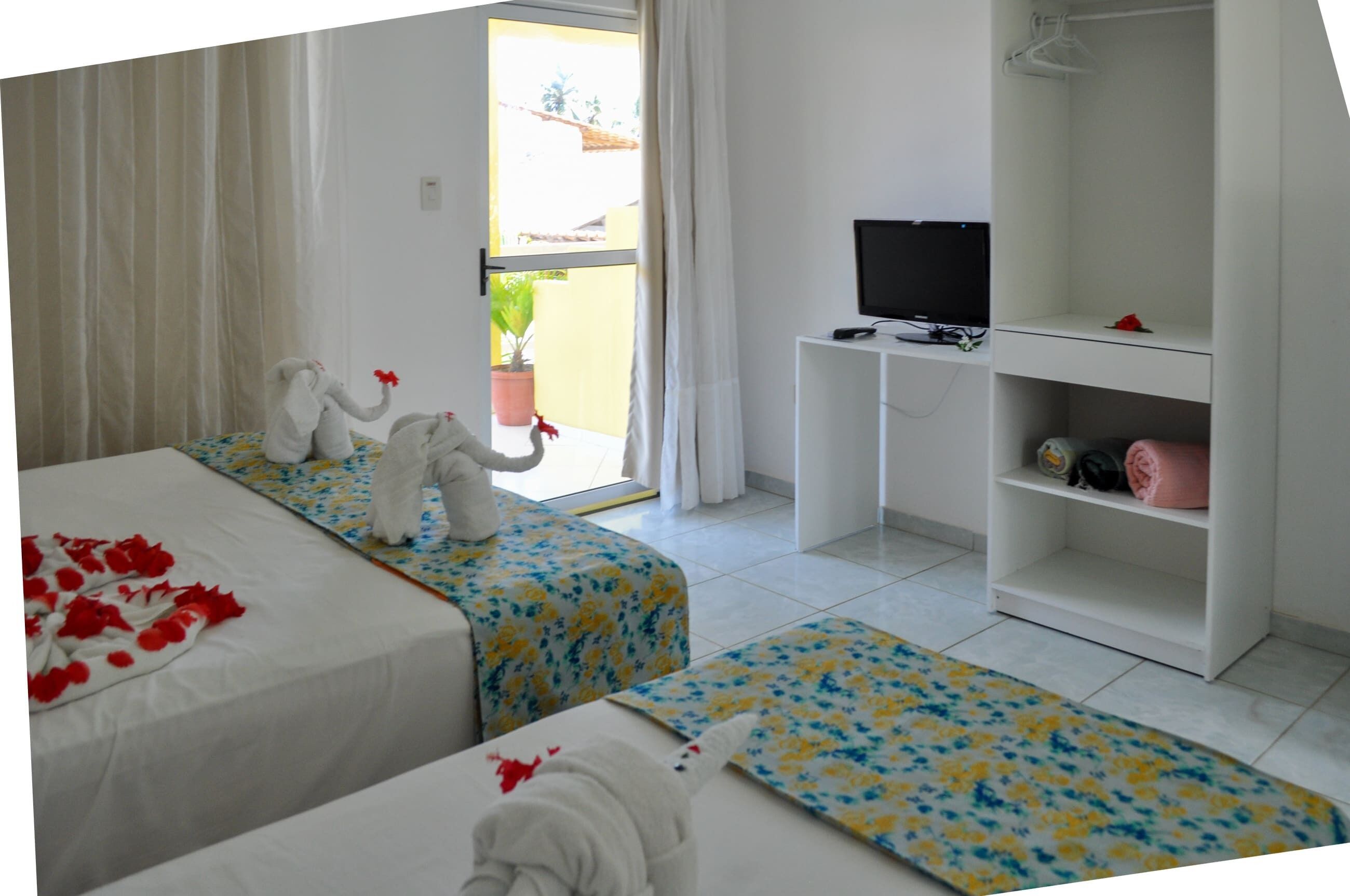 Habitación de hotel con dos camas, televisor, armario y balcón con planta en maceta.