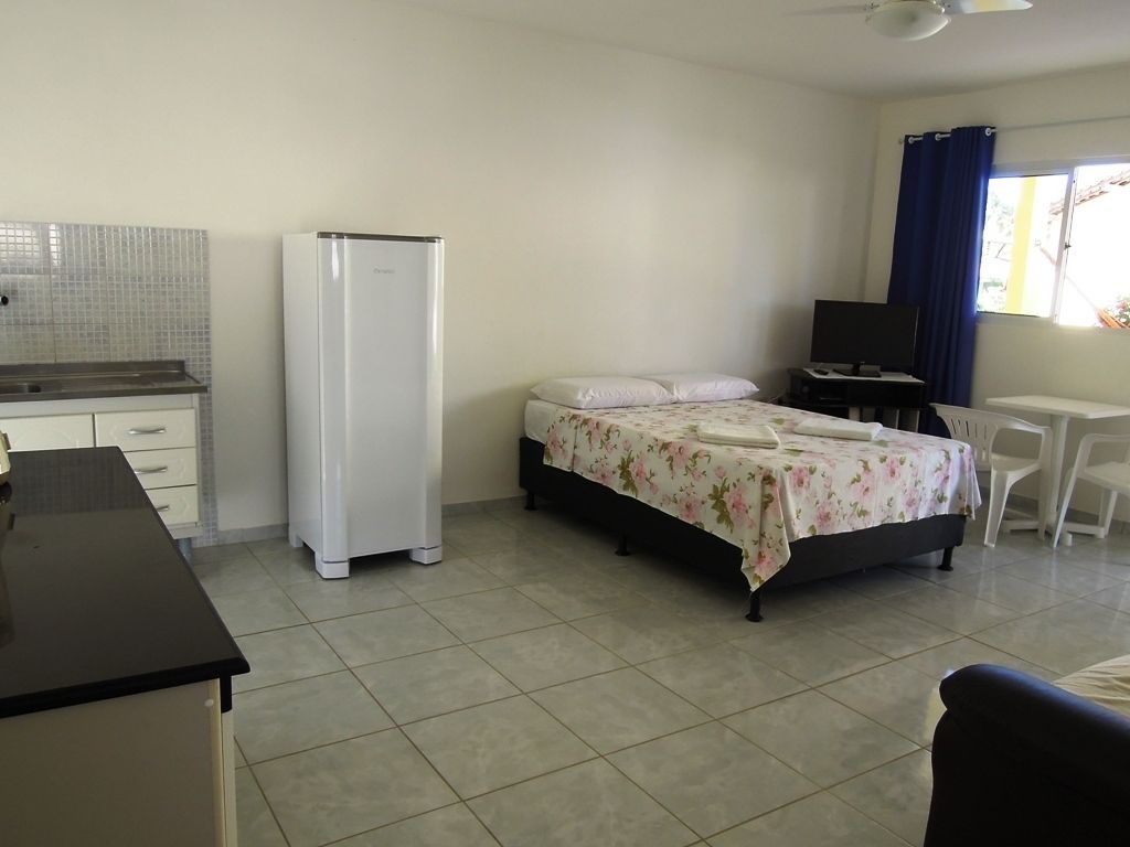 Quarto com cama, escrivaninha, cadeira, televisão e frigorífico.