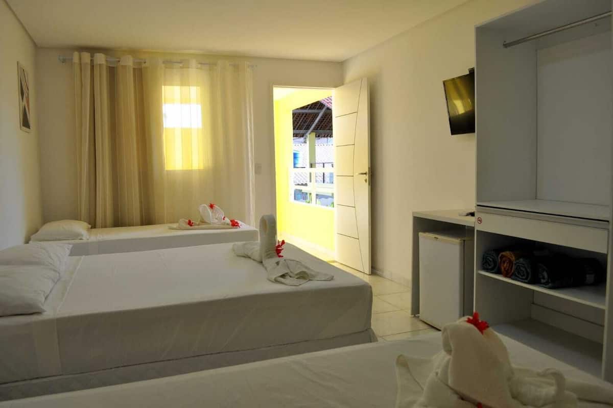 A hotel room with two beds, a wardrobe, and a view of the outside.