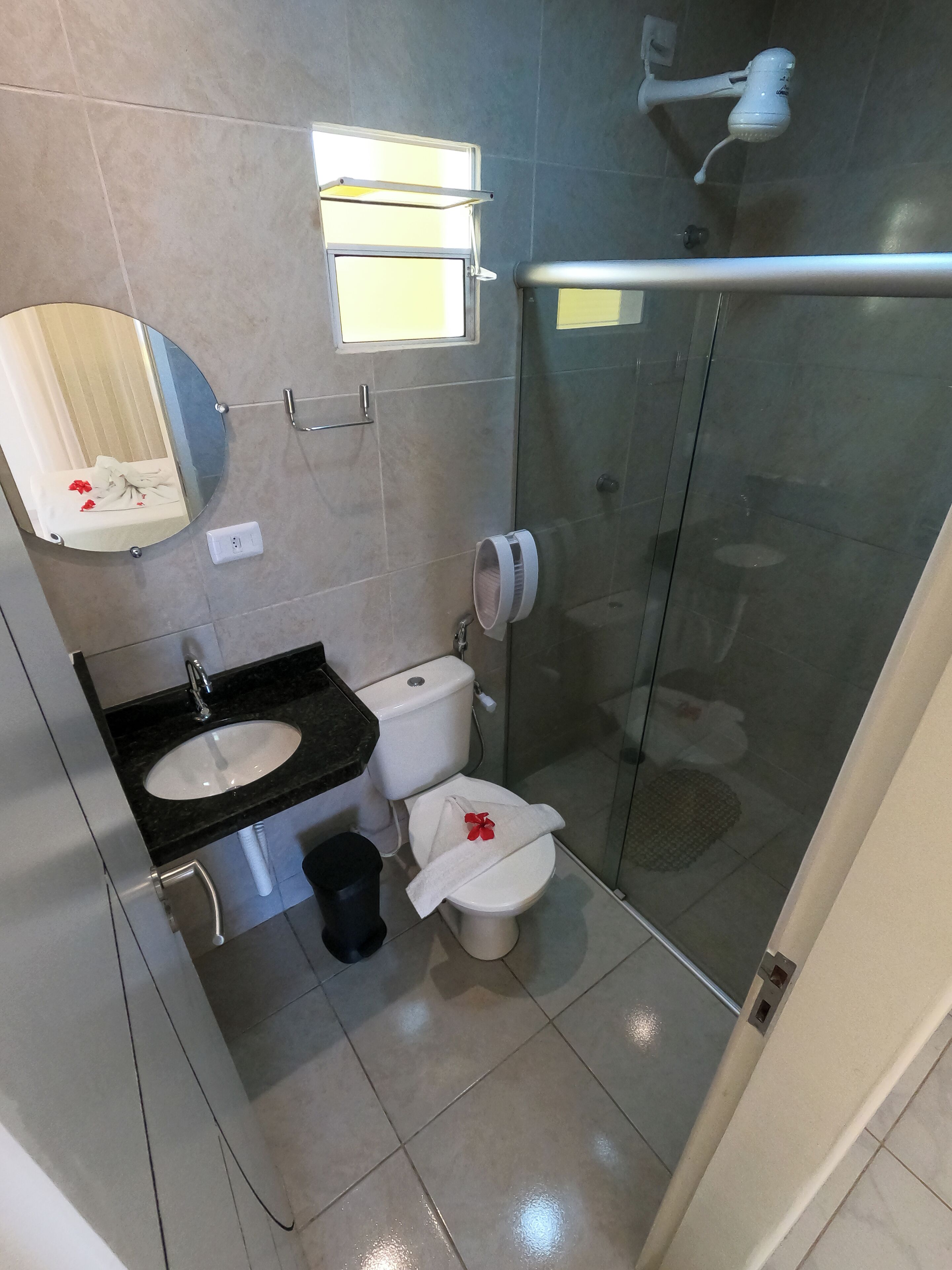 Un baño moderno con cabina de ducha de vidrio, un lavabo con espejo y un inodoro decorado con una toalla y una flor.