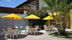 An outdoor patio area with a pool, yellow umbrellas, white plastic chairs, and a tiled floor. - Pousada Jóia Rara (Ipojuca)