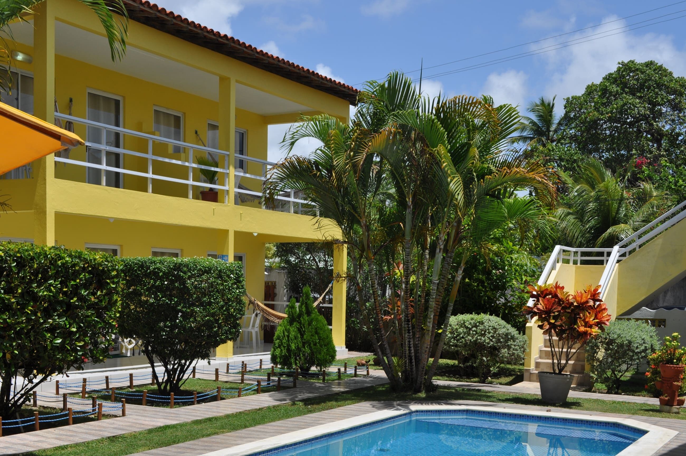 A yellow building with a pool, surrounded by palm trees and potted plants.