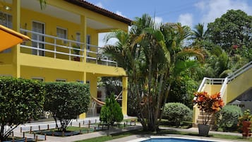 A yellow building with a pool, surrounded by palm trees and potted plants.