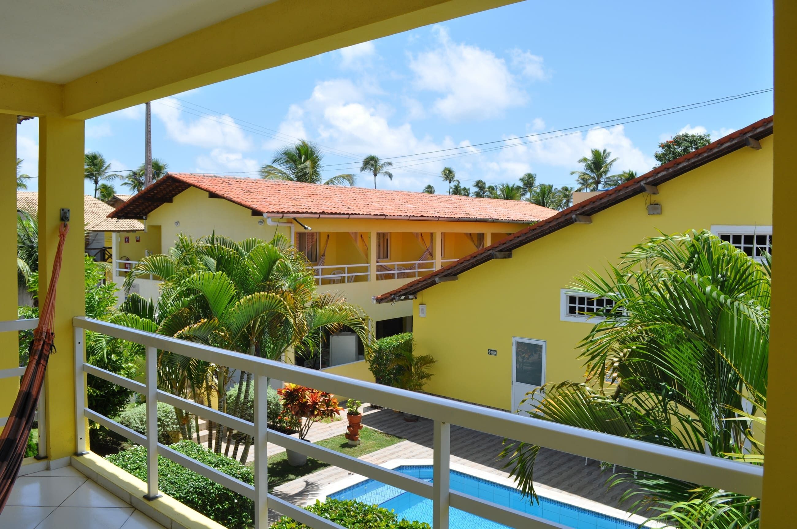 A yellow building with a red roof, surrounded by greenery and a swimming pool.