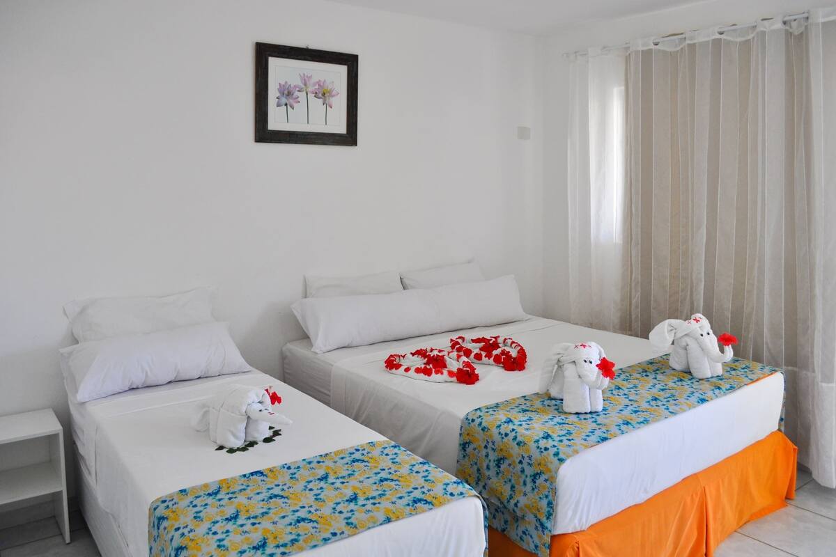 A hotel room with two beds, each with a floral bedspread, white bedding, and a small elephant plush toy.