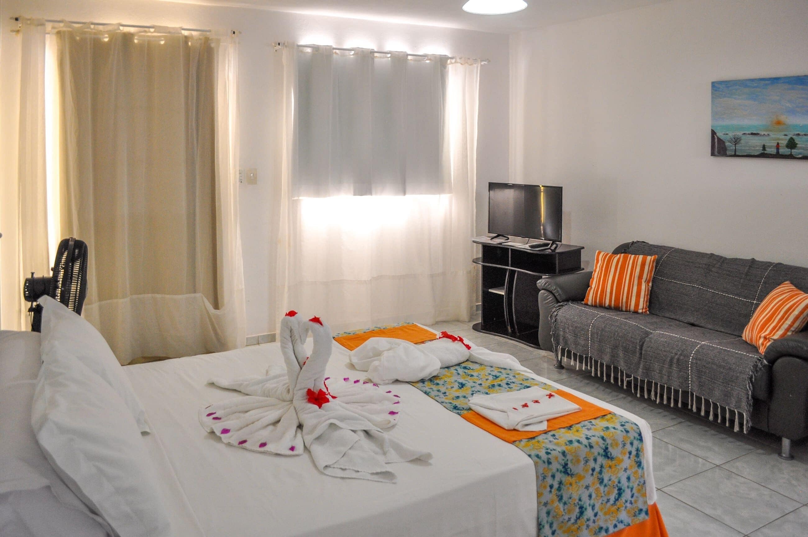 A hotel room with a bed, a sofa, a TV, and a painting on the wall.