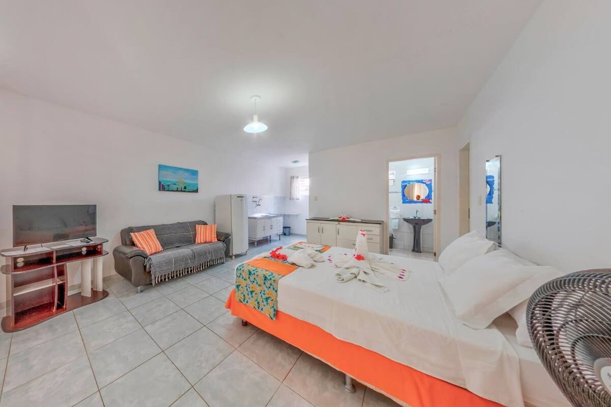 A hotel room with a bed, a desk, a sofa, a TV, a bathroom, and a small kitchen area.