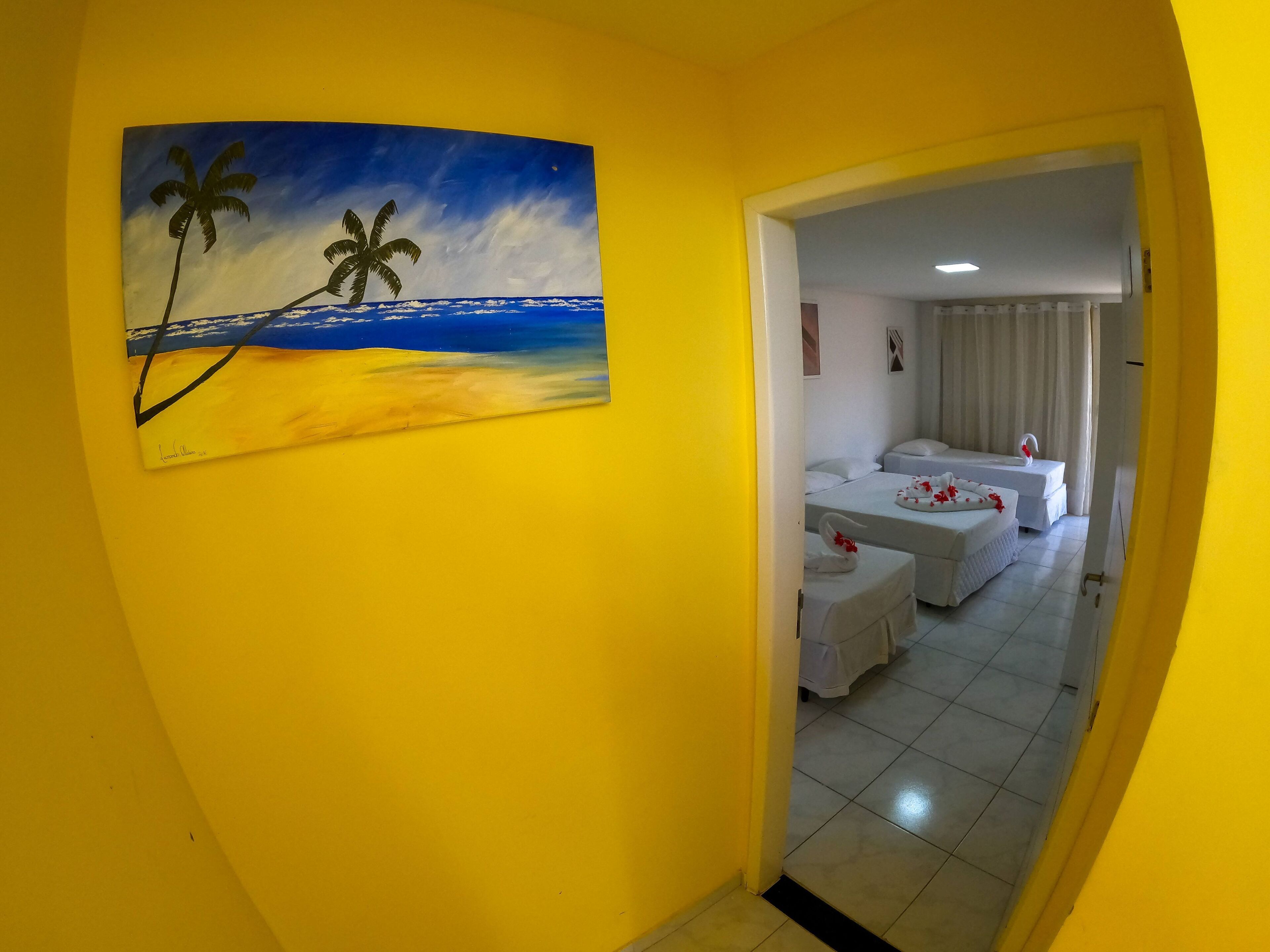 A hotel room with a painting of a beach scene, a bed with white bedding, and a small table with a decorative item.