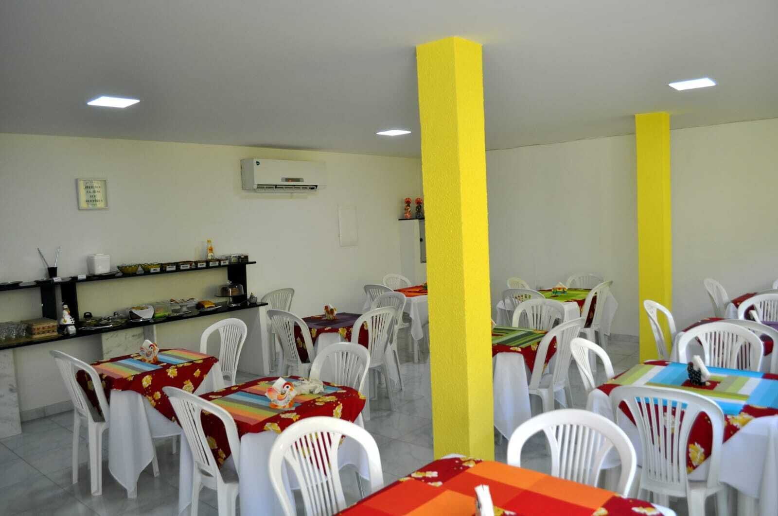 Un comedor con sillas y mesas blancas, pilares amarillos y un equipo de aire acondicionado en la pared.