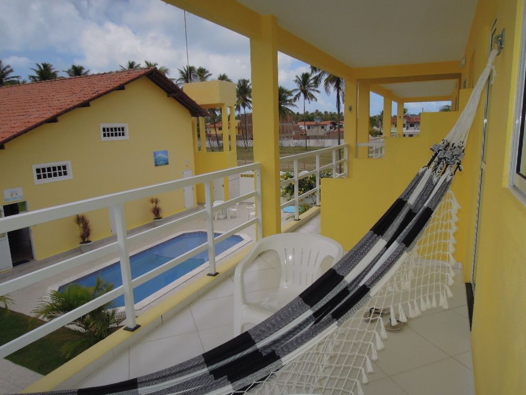 A yellow building with a balcony, a hammock, and a pool.