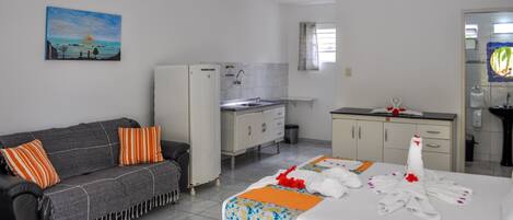 A hotel room with a bed, a sofa, a kitchenette, and a painting on the wall.