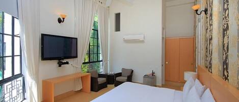 Habitación de hotel con cama, televisor, ventilador de techo, banca y una pequeña mesa.