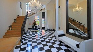 A hotel lobby with a checkered floor, a staircase with a chandelier, and a large mirror reflecting the staircase. - Hotel Republicano 1910 (Girardot)