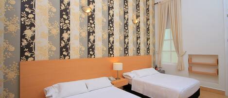 Habitación de hotel con dos camas, cabecera de madera, mesita de noche con lámpara, ventana con cortinas y pared con papel tapiz floral.
