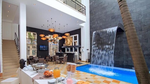 A modern hotel lobby with a dining area, a waterfall feature, and a pool. - Hotel Republicano 1910 (Girardot)
