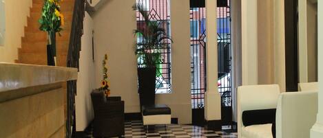 A lobby with a checkered floor, a staircase, a reception desk, and a seating area with a plant and a chair.