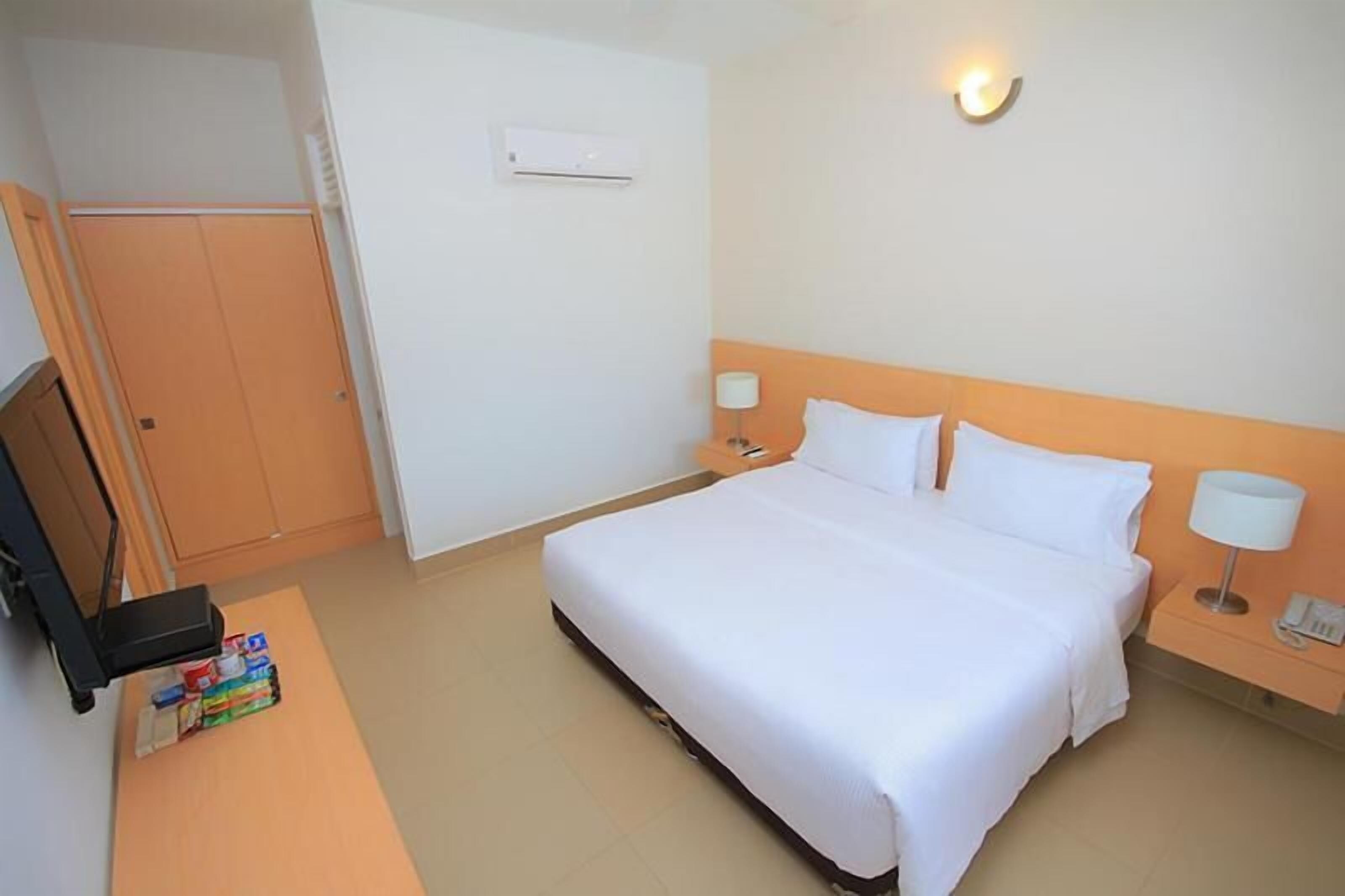 Camera d'albergo con un letto, comodini, una scrivania con sedia, un armadio e un condizionatore d'aria.