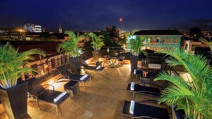 An outdoor patio area with lounge chairs and tables, surrounded by potted plants, under a night sky. - Hotel Republicano 1910 (Girardot)
